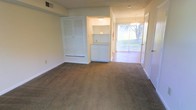 This two-floor residential space offers a practical and well-organized layout designed for comfortable everyday living. The main living area is finished with wall-to-wall carpeting that adds warmth underfoot, and features a set of classic louvered bi-fold closet doors providing ample built-in storage. A built-in nook with cabinetry offers additional organizational convenience, seamlessly integrated into the wall for a clean, uncluttered look. The space opens toward a dining area illuminated by a decorative chandelier, lending a touch of elegance to the area. A full-length sliding glass door allows natural light to pour into the interior while offering direct views of the greenery outside, creating a bright and inviting atmosphere. Vertical blinds along the sliding door provide privacy and light control as needed. Neutral-toned walls and carpeting throughout give the space a versatile, move-in-ready aesthetic. The two-floor layout provides a sense of separation between living and other functional areas of the home, adding to the overall spaciousness and livability of the property.