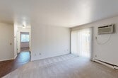 This single-floor, 2-bedroom, 1-bathroom unit offers a practical and comfortable layout with a clean, neutral aesthetic throughout. The combined living and dining area is bright and open, featuring plush carpeting, white walls, and a sliding glass door with vertical blinds that floods the space with natural light and provides access to the outdoors. A wall-mounted air conditioning unit and baseboard heating ensure year-round comfort. The galley-style kitchen is efficiently designed with warm wood cabinetry, dark granite-style countertops, wood-look vinyl flooring, and stainless steel appliances including a refrigerator and dishwasher. Both bedrooms are carpeted and feature ceiling fans with light fixtures. The primary bedroom includes a closet, while the second bedroom benefits from a window with views of surrounding greenery and its own closet with built-in shelving. The full bathroom is clean and functional, offering a double-sink vanity with a wood cabinet base, a tub/shower combo, wood-look flooring, and brushed nickel fixtures. Additional storage is provided by two closets throughout the unit, and a small hardwood-floored entryway nook offers a convenient transition space upon entry.