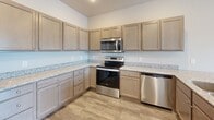 This single-story, two-bedroom, two-bathroom unit is efficiently laid out to maximize functionality within a compact footprint. The combined kitchen and living area serves as the central hub of the unit, with the kitchen offering warm-toned cabinetry, granite-style countertops, and a full suite of stainless steel appliances including a range, over-the-range microwave, and dishwasher. Wood-look plank flooring runs throughout the main living areas, contributing to a cohesive, contemporary aesthetic.

A hallway connects the main living space to the private areas of the unit, passing a dedicated laundry closet housing a stacked washer and dryer. Three closets provide ample storage throughout. The primary bedroom features a ceiling fan, exposed HVAC ductwork adding an industrial accent, and a sliding glass door opening to a private balcony with exterior views. The secondary bedroom is carpeted, also includes a ceiling fan with similar ductwork detail, and benefits from natural light through a large window. Both bathrooms are finished with wood-look tile flooring; one includes a full tub-shower combination with chrome fixtures, while the other features a walk-in shower and vanity with ample counter space.