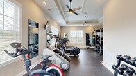 This dedicated fitness center is a comprehensively outfitted single-floor space designed to support a full range of workout routines. The room features elegant tray ceilings with crown molding, recessed lighting, and dual ceiling fans that keep the space comfortable during intense training sessions. Speckled rubber flooring covers the main workout area, providing durability and impact absorption, while a section near the entrance transitions to hardwood-style flooring with interlocking foam mats.

The cardio zone is well-stocked with multiple treadmills, elliptical trainers, a StairMaster, and a Spirit cycling bike, offering a variety of aerobic training options. A wall-mounted flat-screen television is positioned for viewing during cardio sessions. The strength training area includes a multi-station cable machine, a dedicated weight bench, an Everlast heavy punching bag, kettlebells, medicine balls, and a full rack of dumbbells — accommodating everything from functional training to powerlifting.

Full-length mirrors are strategically placed throughout the space, enhancing the sense of openness and allowing for form checks during exercise. Natural light streams in through multiple windows with plantation shutters, offering views of the surrounding greenery. A compact refrigerator near the entrance provides convenient hydration access, rounding out a thoughtfully designed, professional-grade fitness environment.