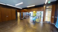 This single-level fitness studio offers a clean, contemporary design with a welcoming and functional layout. The open floor plan provides ample space for a variety of exercise activities, from stretching and yoga to group fitness classes. The flooring features wood-look planks that lend warmth to the space while remaining durable and easy to maintain.

The studio is lined with full-length mirrors along one wall, enhancing the sense of depth and allowing users to monitor their form during workouts. Warm wood-panel wall accents complement the neutral ceiling, which is fitted with recessed and linear LED lighting that ensures the space is well-lit throughout. A wall-mounted flat-screen TV provides entertainment or instructional content during sessions.

A well-organized equipment rack holds an assortment of fitness accessories, including stability balls in multiple sizes, a BOSU balance trainer, and various other training tools. Step platforms are neatly stacked near the mirrored wall for easy access. An adjacent doorway leads to a secondary area, adding to the overall versatility of the space. Large windows visible in the mirror's reflection suggest proximity to natural light sources and urban surroundings.