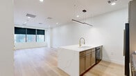 Located on the 8th floor in the heart of downtown Dallas, this thoughtfully designed one-bedroom, one-bathroom residence offers a refined urban living experience. Light oak hardwood flooring flows throughout, complementing a clean, contemporary palette of crisp white walls and modern recessed lighting.

The open-concept living, dining, and kitchen area serves as the centerpiece of the home. The kitchen is outfitted with a stunning marble-topped island featuring a gold-accented faucet and integrated sink, sleek gray cabinetry with brass hardware, premium stainless and black appliances including a professional-grade range, and a built-in refrigerator. Dramatic linear pendant lighting anchors the space above the island.

The spacious bedroom enjoys floor-to-ceiling windows framing striking panoramic views of the Dallas skyline, with blackout roller shades for added versatility. A generous walk-in closet provides ample storage with built-in shelving.

The bathroom exudes luxury with marble tile flooring, a glass-enclosed shower with bold brass fixtures, a lighted vanity mirror, and gray cabinetry. Additional conveniences include a dedicated laundry area and utility room. The overall ambiance is polished, modern, and sophisticated.