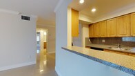 Unit A205 is a single-floor residence finished with polished large-format tile flooring that runs consistently throughout the space, contributing to a clean, cohesive aesthetic. The living area is bright and open, featuring crown molding, a ceiling light fixture, and a sliding glass door fitted with vertical blinds that allows generous natural light and outdoor views. An adjacent dining area connects seamlessly to the kitchen via a pass-through window, enhancing the open feel of the shared living spaces.

The kitchen is designed in a galley configuration, offering ample storage through warm-toned wood cabinetry that lines both walls from floor to ceiling. Granite-style laminate countertops and a textured tile backsplash complement the stainless steel refrigerator. Recessed lighting illuminates the workspace effectively.

The bedrooms are well-proportioned, each featuring ceiling fans, vertical blind-covered windows with exterior views, and the same polished tile flooring. The bathroom is outfitted with a wood-finish vanity, a wide mirror with overhead lighting, and a full tub-shower combination surrounded by neutral tile walls and a built-in niche. Overall, the unit presents a functional and well-maintained interior with a light, airy ambiance throughout.