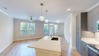 Located at 7630 Knightdale Boulevard in Knightdale, NC, this well-appointed 2-bedroom, 2-bathroom single-floor residence combines modern design with functional living. The open-concept kitchen and living area serves as the heart of the home, anchored by a sleek center island with a built-in sink and pendant globe lighting overhead. The kitchen features gray flat-front cabinetry extending to the ceiling, white quartz countertops, a subway tile backsplash, stainless steel appliances, and recessed lighting — a cohesive and contemporary aesthetic throughout. The living room benefits from large windows that frame views of surrounding greenery, allowing natural light to fill the space. A ceiling fan adds comfort to the area. Both bedrooms are generously proportioned, each with large windows overlooking lush tree canopy, hardwood-style flooring, and ceiling fans. The spacious primary bedroom connects to a well-designed en-suite bathroom featuring gray cabinetry, white countertops, and a walk-in closet outfitted with built-in shelving, hanging rods, and drawer units. The second bathroom is equally well-finished. Consistent light hardwood-style flooring and neutral wall tones flow throughout the entire residence, creating a bright, cohesive, and move-in-ready living environment.