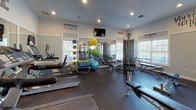 Located at 1555 Village Center Dr in Lakeland, Florida, this single-floor fitness center is a well-equipped facility designed to support a comprehensive workout routine. The space features rubber-floored exercise areas bathed in natural light from multiple windows dressed with white blinds, creating a bright and energizing atmosphere complemented by recessed ceiling lighting.

The cardio zone is outfitted with multiple treadmills and a stationary bike, each equipped with individual screens for entertainment during workouts. A dedicated strength training area houses a cable crossover machine, a multi-functional weight rack, and an assortment of resistance machines suited for both upper and lower body exercises. A full dumbbell rack with a wide range of weights, stability balls, and various fitness accessories provide ample options for functional and free-weight training.

Large wall-mounted mirrors throughout the space enhance the sense of openness and allow users to monitor their form. Mounted televisions offer additional entertainment. The walls are adorned with motivational phrases such as "You've Got This," "Everyday is a Good Day to Work Out," and "The Pain You Feel Today is the Strength You Feel Tomorrow," contributing to an upbeat and encouraging environment. The fitness center is accessed through glass-paneled French doors, adding an elegant touch to this practical and fully appointed facility.