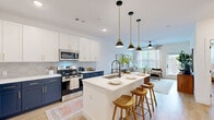 This thoughtfully designed single-floor residence offers a seamless open-concept layout that connects the kitchen, dining, and living areas into one cohesive, light-filled space. Light wood-tone flooring flows throughout, complementing the clean white walls and modern finishes.

The kitchen is a standout feature, showcasing a bold two-tone design with navy lower cabinets and crisp white upper cabinetry, accented by a geometric tile backsplash and white quartz countertops. A central island with a waterfall edge provides bar seating for three, illuminated by a trio of pendant lights with brass hardware. Stainless steel appliances complete the space.

The living room benefits from large windows that invite an abundance of natural light, with a ceiling fan adding both function and style. The bedroom offers a comfortable, well-proportioned retreat with light-toned walls, wood flooring, and a dedicated closet.

The bathroom features full-height tile surrounding a soaking tub and shower combo, with matte black fixtures adding a contemporary touch. A dedicated laundry room houses a full-size washer and dryer with overhead shelving for added convenience. A hallway connects all areas efficiently, making excellent use of the overall footprint.