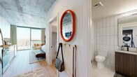 Located at 50 E Fillmore St in the heart of Phoenix, AZ, this thoughtfully designed studio offers an efficient yet stylish urban living experience. The open-concept layout seamlessly integrates the kitchen, living, and sleeping areas beneath a striking exposed concrete ceiling that lends an industrial-chic character throughout.

The kitchen is outfitted with crisp white cabinetry, quartz countertops, a tiled backsplash, and a full suite of stainless steel appliances including a range, refrigerator, dishwasher, and built-in microwave — all arranged in a clean galley configuration. Light wood flooring flows throughout the main living area, enhancing the sense of warmth and continuity.

Floor-to-ceiling windows flood the space with abundant natural light while framing expansive views of the Phoenix skyline, creating a bright and airy ambiance. A built-in sleeping nook provides a defined bedroom area, complemented by generous closet storage.

The unit features two bathrooms — one with large-format tile flooring, bold white subway wall tile, and a wood-toned vanity, and a second more compact bath. In-unit laundry adds everyday convenience. A welcoming entry with a decorative mirror and wall hooks completes this well-appointed urban residence.