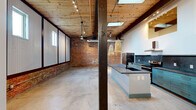Located at 1812 Slaton Street in Augusta, GA, this single-floor, 3-bedroom, 2-bathroom home delivers a bold industrial aesthetic with thoughtfully curated modern touches. The open-concept living and kitchen area serves as the heart of the home, featuring soaring wood-plank ceilings with exposed dark beams, skylights that flood the space with natural light, and polished concrete floors that extend throughout. Exposed brick walls add raw character, while corrugated metal wall panels and dark structural columns lend an authentic warehouse-inspired feel. A large kitchen island with a granite countertop and teal cabinetry anchors the kitchen, complemented by a dark tile backsplash, stainless steel appliances, and woven pendant lighting. The spacious primary bedroom offers generous room, with crisp white walls and polished concrete floors maintaining the cohesive aesthetic. The two bathrooms are consistently appointed with teal vanity cabinets, granite countertops, black matte fixtures, round gold-framed mirrors, and tiled shower surrounds. Additional rooms include dedicated closets, a hallway, and bedrooms that share the same clean, minimalist design. Track lighting and ceiling fans are featured throughout, enhancing both function and style in this distinctive Augusta residence.