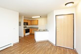This single-floor residence offers a practical and comfortable layout designed for everyday living. The open entry area flows into a spacious living room finished with warm hardwood-style flooring and a sliding glass door that floods the space with natural light while providing access to an outdoor balcony area. Baseboard heating is present throughout, ensuring consistent comfort year-round.

The kitchen is well-equipped with an L-shaped layout featuring warm wood cabinetry, gray laminate countertops, and a full suite of appliances including an electric range, over-the-range microwave, dishwasher, and refrigerator. Hardwood-style flooring continues through the kitchen, which also benefits from overhead fluorescent lighting.

The bedrooms are carpeted for warmth and comfort, each featuring large windows that invite natural light and outdoor views of surrounding greenery. Ceiling fans provide additional ventilation. One bedroom includes a generously sized walk-in closet with built-in shelving and hanging rods, offering excellent storage capacity.

The bathroom is clean and functional, featuring a wood-toned vanity with a gray countertop, a mirrored medicine cabinet, and hardwood-style flooring. A full bathtub and shower are also included. Throughout the residence, light wood trim and neutral wall tones contribute to a cohesive, understated aesthetic.