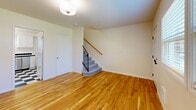 This three-floor unit at 10381 SW Eastridge St in Portland, Oregon, offers a well-organized layout distributed across a ground-level entry, a main living floor, and an upper bedroom level. The entry level houses a spacious utility room with an in-unit washer and dryer, featuring exposed insulated ductwork overhead and a concrete floor, providing practical storage and laundry functionality.

The main floor is the most active level, containing the kitchen and primary living area. The kitchen features a classic black-and-white checkered floor, white shaker-style cabinetry, black tile backsplash accents, white countertops, and stainless steel appliances including a refrigerator, electric range, and dishwasher. A window brings in natural light. The adjoining living area showcases warm hardwood flooring and a staircase with a black metal railing leading to the upper floor.

The upper level contains the bedroom, which is comfortably sized with hardwood floors, a window offering outdoor views, and multiple closet doors providing ample storage. Two full bathrooms serve the unit: one features a white vanity, mirror with vanity lighting, and speckled tile flooring; the other includes a tub/shower combo with white subway tile surround and a white vanity with stone-look countertop.