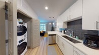 Located at 3883 S Moody Ave in Portland, Oregon, this thoughtfully designed single-floor unit offers a cohesive blend of modern finishes and functional living. The open-concept kitchen flows seamlessly into the living area, creating an efficient and welcoming layout. The kitchen is outfitted with white shaker-style cabinetry, quartz countertops, a stainless steel sink, and a full suite of stainless steel appliances including a refrigerator, electric range, built-in microwave, and dishwasher. A striking dark slate tile backsplash adds a bold contrast to the bright cabinetry. Pendant lighting above the kitchen peninsula provides warm task lighting while reinforcing the modern aesthetic. Light-toned hardwood-style flooring runs throughout, lending continuity to the space. The living area is bathed in natural light from a large picture window with views of surrounding greenery. The bedroom features a generous sliding-door closet, a wall-mounted mini-split system, and continues the light flooring palette. The bathroom is finished with a dark wood floating vanity, quartz countertop, a large framed mirror, and clean white walls. A stacked washer and dryer unit is conveniently integrated near the kitchen, completing this well-equipped and contemporary living space.