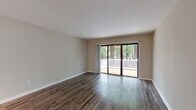 Located at 104 Landmark Ct in Newport News, VA, this single-floor, 2-bedroom, 1-bathroom home offers a well-organized layout with a comfortable and functional design. The combined living and dining area is a central highlight, featuring rich hardwood-style flooring and a large sliding glass door that opens to a deck overlooking a lush, wooded backdrop, filling the space with natural light and serene outdoor views.

The kitchen is thoughtfully appointed with white cabinetry, granite-patterned countertops, a peninsula with pendant lighting, and white appliances including a range, microwave, and refrigerator. A pantry and dedicated laundry area add to the home's practical conveniences.

Both bedrooms are carpeted for comfort, with the primary bedroom offering a generous walk-in closet with built-in shelving and a window framing green tree views. The second bedroom also features neutral tones and ample ventilation. Five closets throughout the home provide abundant storage.

The bathroom is clean and straightforward, featuring a full tub-shower combination with brushed nickel fixtures and hardwood-style flooring. A hallway connects the main living spaces, completing this efficiently designed single-level home.