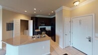 This single-floor residence is designed with a functional and cohesive layout that connects its key living spaces seamlessly. The kitchen is a standout feature, outfitted with rich dark espresso cabinetry that extends to the ceiling and is accented by white crown molding. A tile backsplash adds texture behind the countertops, while black appliances — including a full-size refrigerator, range, and microwave — complement the cabinetry's dark tones. Light tile flooring runs throughout the kitchen and entry areas, and a peninsula with a stainless steel sink and granite-style countertops provides additional workspace and casual dining potential. Recessed lighting illuminates the kitchen efficiently.

The living area features soft carpeting and is brightened by a set of French doors that invite natural light and provide outdoor access. Crown molding and a ceiling fan add architectural detail and comfort to the room. Neutral warm-toned walls run throughout, creating a consistent and inviting ambiance.

The bathroom includes a dual-sink vanity with warm wood-toned cabinetry, a large wall mirror, and a tub-shower combination with decorative tile accents and a curtain rod. The overall design prioritizes practicality while maintaining a clean, classic aesthetic throughout the space.