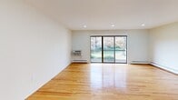 Located at 1001 Blue Spring Rd in Princeton, NJ, this multi-floor residence spans three levels and offers a clean, functional layout with a neutral palette throughout. The entry foyer welcomes visitors through a white paneled door with a sidelight window, providing a glimpse of the exterior surroundings and offering a secure, chain-lock entry point.

The main living area is expansive and bright, anchored by warm hardwood flooring that runs throughout much of the home. Recessed lighting illuminates the space, while a full-width sliding glass door opens onto a private balcony overlooking landscaped greenery—bringing natural light deep into the interior. Wall-unit air conditioning and baseboard heating provide year-round climate comfort.

The kitchen is outfitted with white shaker-style cabinetry, light quartz countertops, a white subway tile backsplash, and stainless steel appliances including a range, built-in microwave, and dishwasher. A matte black faucet adds a contemporary contrast.

Bedrooms feature gleaming hardwood floors, generous closet space with built-in rods and shelving, and windows with slatted blinds. The bathroom is finished with large-format marble-style tile, a glass-enclosed shower with a matte black rainfall fixture, a vanity with a white basin, and tile flooring.