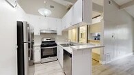 Located at 1100 Fairhaven Ave in Santa Ana, CA, this single-floor unit offers a well-designed layout making smart use of its space. Light wood-style flooring flows consistently throughout, creating a cohesive and airy feel across every room.

The kitchen is a standout feature, equipped with stainless steel appliances including a gas range, dishwasher, and refrigerator. Crisp white cabinetry extends to the ceiling, complemented by granite-style countertops and a peninsula that opens toward the living area. Vaulted ceilings with exposed beams and a pendant light add architectural character to this space.

The living room benefits from vaulted ceilings and a ceiling fan, with sliding glass doors that lead to a private balcony and bring in natural light and outdoor views. Neutral-toned walls provide a clean, versatile backdrop throughout.

The bedroom is a comfortable size, featuring a wall-mounted AC unit, a large window with vertical blinds that invite natural light, and mirrored sliding closet doors that enhance the sense of space. Additional closets are accessible from the hallway.

The bathroom is cleanly appointed with a granite-topped vanity, white cabinetry, mirrored medicine cabinets, and a full tub-shower combination, all finished with light wood-style flooring for a consistent aesthetic.