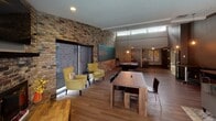 Located at 512 Harold Dr in Burnsville, Minnesota, this single-floor facility is thoughtfully designed to accommodate a variety of activities and social functions. The space blends modern finishes with industrial character, creating an engaging and functional environment throughout.

A long, well-lit corridor with light tile flooring and neutral gray walls serves as the central spine of the space, connecting each area seamlessly. Pendant lighting runs the length of the hallway, providing consistent illumination and a clean, contemporary feel.

The fitness areas are a standout feature of this space. A dedicated exercise studio is equipped with wall-to-wall mirrors, hardwood-style flooring, stability balls, and wall-mounted mats, making it suitable for a range of workout activities. An adjacent cardio room features treadmills and stationary bikes set against a striking exposed brick wall accented with a bold geometric mural.

The social lounge area offers a warm and inviting atmosphere with wood-look flooring, dark accent walls, pendant globe lighting, and comfortable seating arrangements. A game room with a pool table and yellow accent chairs adds a recreational dimension, benefiting from natural light through clerestory windows.

A kitchenette with dark cabinetry, a double sink, open shelving, and a textured tile backsplash rounds out the space, supporting event and gathering use.