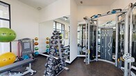 This dedicated exercise room is a compact yet fully outfitted fitness facility designed to support a well-rounded workout routine. The space features durable rubber flooring throughout, providing a safe and practical surface suited for a wide range of activities. Large, floor-to-ceiling black-framed windows line multiple walls, flooding the room with abundant natural light and offering views of lush outdoor greenery and a nearby pool area, creating an energizing atmosphere for exercise.

The cardio zone is equipped with treadmalls, an elliptical trainer, and a stationary bike, all positioned to take advantage of the outdoor views. Ceiling fans overhead help maintain airflow and comfort during workouts. Wall-mounted flat-screen televisions provide entertainment options for users.

The strength training area includes a tiered dumbbell rack with a full range of free weights, a collection of medicine balls and resistance bands, a Matrix adjustable weight bench, and a multi-station cable machine that supports a variety of strength exercises. Large mirrors are strategically placed to maximize the sense of space and allow for proper form checks during training. Motivational signage adorns the walls, contributing to an upbeat and focused environment. A glass door provides direct access to the outdoor area.