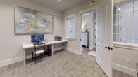This single-floor business center is designed to provide residents or guests with a functional and polished workspace. The room features built-in white laminate desks that run along two walls, offering ample surface area for computing and administrative tasks. Each workstation is equipped with a desktop computer, and a multifunction printer/scanner is conveniently accessible on the shared work surface.

The space is finished with neutral gray walls, crown molding, and patterned low-pile carpeting that adds subtle texture underfoot. Recessed lighting provides consistent illumination throughout the room, while a framed abstract artwork in soft blues, yellows, and whites adds a decorative focal point above the primary workstation. A window allows for a degree of natural light.

A prominent Luxer One smart package locker system occupies a dedicated area of the space, offering secure, automated package retrieval. The matte black locker bank contrasts neatly against the light walls and coordinates with the room's understated, contemporary design.

Accessed through a paneled white door, the business center connects to adjacent hallways, suggesting it functions as part of a larger amenity suite. Overall, the space balances practicality with a clean, welcoming aesthetic.