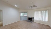 This single-story residence offers a well-organized layout with a neutral color palette of soft whites and warm beige tones throughout. The living room serves as the central gathering space, highlighted by a stone-tiled fireplace surround that anchors the room as a focal point. A ceiling fan is mounted overhead, and sliding glass doors dressed with vertical blinds provide direct outdoor access and fill the space with natural light. The open sightlines connect the living area to an adjacent room, which also features a ceiling fan and its own sliding glass door to the exterior.

The kitchen is accessed via a pass-through opening with a raised counter, offering light wood cabinetry, white appliances including a refrigerator and dishwasher, a double-basin sink, and tile flooring. A dedicated bedroom features a ceiling fan, large window with outdoor views, and access to a spacious walk-in closet equipped with built-in shelving and dual hanging rods. Two bathrooms serve the residence — one with a shower stall and vanity, and another with a tub-shower combination — both finished with light tile flooring and clean, functional fixtures throughout.