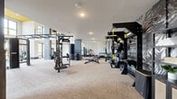 This contemporary two-floor fitness facility offers a comprehensive workout environment designed with both functionality and aesthetics in mind. The ground floor serves as the primary fitness area, featuring patterned carpet flooring and an extensive array of strength and cardio equipment, including cable machines, punching bags, rowing machines, ellipticals, stationary bikes, and multi-use training rigs. Bold tropical-print accent walls punctuate the space alongside large-format mirrors that amplify the sense of openness. Natural light flows in generously through large black-framed windows, and recessed lighting ensures consistent illumination throughout. A sleek steel staircase with cable railings connects the two floors, adding an industrial-modern touch. The upper floor continues the cardio-focused layout, with rows of machines positioned near windows that offer exterior views, and features a distinctive yellow ceiling accent that adds a vibrant design element. Adjacent to the main floor is a dedicated studio space finished with light hardwood flooring, full-length mirrored walls, a wall-mounted TV, ballet barre, and glass-panel partitions, making it ideal for group classes or individual training sessions. Together, the two floors create a well-rounded, spacious fitness environment with a polished, modern design.