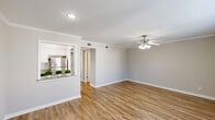 Located at 10004 Regal Park Ln in Dallas, TX, this well-appointed single-story home offers one bedroom and three bathrooms within a thoughtfully designed layout. The open-concept living and dining area is bright and welcoming, featuring warm hardwood-style flooring, crisp white crown molding, a ceiling fan with light fixture, and recessed lighting. A pass-through window connects the living space to the kitchen, creating an airy, connected feel throughout. The kitchen is outfitted with white shaker-style cabinetry, granite countertops, subway tile backsplash, stainless steel appliances including a refrigerator and electric range, and a stainless steel sink — combining modern style with functional design. The generously sized primary bedroom benefits from natural light streaming through large windows with views of the outdoors, complemented by its own ceiling fan. The bedroom is serviced by multiple bathrooms, including one featuring a tiled tub-shower combination. A hallway connects the various rooms, with closet storage also available. Neutral gray wall tones throughout lend a clean, cohesive aesthetic, making this Dallas home a comfortable and move-in-ready space.