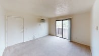 This single-floor unit offers a straightforward and functional layout designed for comfortable everyday living. The living area is spacious and bright, featuring neutral-toned carpet, a textured ceiling, and a wall-mounted air conditioning unit. Sliding glass doors open directly onto a private balcony, providing outdoor views of surrounding greenery and allowing natural light to fill the space. Vertical blinds offer privacy and light control.

The bedrooms are carpeted and finished with neutral walls and textured ceilings. Each room includes a window overlooking the outdoors, with views of trees and the surrounding landscape. Flush-mount ceiling fixtures provide overhead lighting, and standard electrical outlets are conveniently placed throughout.

The galley-style kitchen features dark wood cabinetry lining both walls, offering ample storage space. Light-toned countertops provide a functional work surface, and the kitchen is equipped with a double-basin sink, a refrigerator, and a range. Tile flooring completes the practical design of this area.

The bathroom includes a full tub and shower combination with a chrome curtain rod, a toilet, a single-basin vanity, and a wall-mounted medicine cabinet with a mirror. Overall, the unit presents a clean, neutral aesthetic throughout.