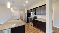 Located at 410 S Noyer Rd in Fort Wayne, Indiana, this single-story home offers a well-designed, open-concept layout that maximizes functionality and comfort. The kitchen serves as a centerpiece of the living area, showcasing rich dark cabinetry, granite-style countertops, a large island with a built-in sink, pendant lighting, and a full suite of stainless steel appliances including a refrigerator, electric range, and over-the-range microwave. The kitchen flows seamlessly into the living and dining areas, which feature durable hardwood-style flooring and natural light from a window overlooking the outdoors. Bedrooms are finished with plush carpeting, ceiling fans, and windows that bring in generous natural light and views of the surrounding neighborhood. Closet space is well-appointed, with a walk-in closet visible in one of the bedrooms. The primary bathroom features a dual-sink vanity with granite countertops, dark cabinetry, a walk-in shower, and hardwood-style flooring. A secondary bathroom provides a full tub and shower combination, a single-sink vanity with matching finishes, and hardwood-style flooring. Neutral wall tones and consistent finishes throughout give the home a clean, cohesive aesthetic.