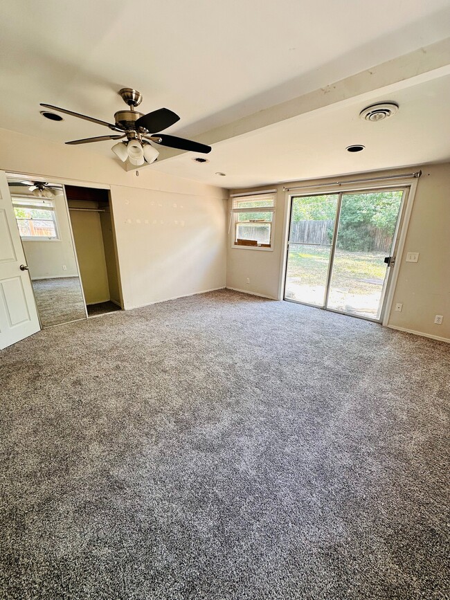 Spacious bedroom with plush carpeting, modern ceiling fan, and abundant natural light through a sliding glass door leading to a serene backyard. - 1385 Yukon Street