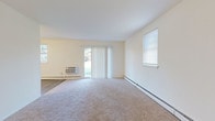 This single-floor residential unit offers a functional and well-organized layout designed for comfortable everyday living. Entry is through a clean, narrow hallway finished with durable wood-look luxury vinyl plank flooring and crisp white trim, setting a tidy tone throughout.

The kitchen is a standout feature, outfitted with white shaker-style cabinetry, a classic subway tile backsplash, and a full suite of white appliances including a gas range, over-the-range microwave, dishwasher, and refrigerator. Light wood-look flooring extends through the kitchen, which is brightened by a flush ceiling light fixture.

Adjacent to the kitchen, the open living and dining area is generously sized, bathed in natural light from a sliding glass door and multiple windows dressed with vertical blinds and horizontal shades. Plush neutral carpeting, baseboard heating, and a wall-mounted air conditioning unit make the space adaptable year-round. A ceiling fan adds comfort overhead.

The bedrooms continue the warm, neutral palette with soft carpeting, ample natural light from windows, and individual climate control units. Each room offers a clean, versatile canvas.

The bathroom is neatly appointed with large-format tile flooring, a tiled tub and shower combination with decorative accent tile, a white vanity with medicine cabinet, and standard fixtures — offering a functional and clean design.