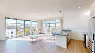 This contemporary residence is designed to maximize natural light and urban views, creating a bright and airy atmosphere throughout. The open-plan living and dining area serves as the heart of the home, featuring light wood-look flooring, crisp white walls, and an expansive wall of floor-to-ceiling windows and sliding glass doors that frame sweeping panoramic city views. These doors open directly onto a private balcony, seamlessly blending indoor and outdoor living.

The kitchen is thoughtfully integrated into the open living space, anchored by a generous island with granite countertops and bar seating. White shaker-style cabinetry, a white subway tile backsplash, stainless steel appliances — including a refrigerator, electric range, and built-in microwave — and pendant lighting complete this well-appointed cooking space.

The bedrooms offer a calm retreat, finished with plush carpeting, individual climate control units, and ample closet storage. One bedroom features a sliding double closet alongside additional door access, providing generous storage options.

The bathroom is cleanly designed with wood-look tile flooring, a granite-topped vanity with an undermount sink, a soaking tub with shower, and crisp white finishes throughout. Every room reflects a cohesive, modern aesthetic suited for contemporary urban living.
