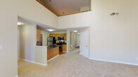 This two-floor residence offers a well-designed layout with a variety of functional spaces throughout. The main living area immediately impresses with its soaring double-height ceilings, creating an open and airy atmosphere. A staircase connects the two levels, and natural light filters through multiple windows across the home.

The kitchen is equipped with stainless steel appliances, including a refrigerator, electric range, and over-the-range microwave. Warm oak cabinetry with raised-panel detailing provides generous storage, complemented by dark granite-style countertops and hardwood flooring. The kitchen also features a dedicated laundry area with hookups nearby.

The spacious living room boasts vaulted ceilings, a classic white fireplace, and large patio doors that invite natural light and outdoor views. Soft carpet flooring runs throughout the living areas and bedrooms, adding warmth and comfort.

The bedrooms are generously sized, each featuring neutral-toned walls, carpeted floors, and windows that bring in natural light. The bathrooms include hardwood flooring, wood-tone vanities, and one full bath with a tub-shower combination. A secondary bathroom features a standalone shower and is conveniently sized.

Overall, the space presents a comfortable and functional layout suited for everyday living across two well-appointed floors.