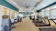 This fitness center in Gulf Breeze, Florida, offers a thoughtfully designed single-floor space built to accommodate a wide range of workout needs. The interior is characterized by elevated ceilings with coffered detailing, teal accent walls contrasting crisp white wainscoting, and large windows that flood the space with natural light, creating an open and energizing atmosphere throughout.

The layout is organized into distinct functional zones. The cardio area lines one side of the room with multiple treadmills and elliptical machines by SportsArt, providing ample equipment for aerobic training. Opposite, a dedicated strength zone houses a selection of selectorized cable and resistance machines suited for full-body training. A separate free-weight area features a full dumbbell rack alongside adjustable benches and a rowing machine, accompanied by floor-to-ceiling mirrors that enhance the sense of space and support proper form. A stretching and functional training section rounds out the facility, stocked with stability balls, resistance accessories, and open floor space for flexibility work.

Oversized ceiling fans in the coffered sections support airflow and comfort during intense sessions. The neutral carpet flooring, recessed lighting, and transom windows contribute to a clean, polished aesthetic. French doors provide convenient access, reinforcing the facility's welcoming and well-maintained character.