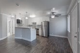 Located at 3670 Peacock Ct in Santa Clara, CA, this one-bedroom, one-bathroom unit offers a thoughtfully designed single-floor layout that maximizes every square foot. The open-concept kitchen and living area serves as the heart of the home, featuring rich hardwood-style flooring, crown molding, and a ceiling fan that enhances airflow and comfort. The kitchen is well-appointed with white shaker cabinetry, a mosaic tile backsplash, stainless steel appliances including a refrigerator, range, microwave, and dishwasher, and a white peninsula island with pendant lighting overhead — ideal for both meal prep and casual dining. The living area flows seamlessly from the kitchen, creating an open and connected feel. The bedroom offers plush wall-to-wall carpeting, a ceiling fan, a window with natural light, and a baseboard heating unit, along with a dedicated closet for storage. The bathroom is finished with wood-look tile flooring, a combined shower and bathtub with sliding glass doors, a white vanity, and an overhead cabinet for additional storage. Neutral gray tones throughout the unit provide a clean, modern aesthetic that is both inviting and versatile.