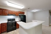 Located at 3900 George Busbee Pkwy NW in Kennesaw, Georgia, this well-laid-out two-bedroom, two-bathroom residence offers a comfortable and functional single-floor living experience. The kitchen is a standout feature, showcasing rich cherry-toned cabinetry, white quartz-style countertops, light wood-look flooring, and black appliances including a range, dishwasher, and refrigerator. A wraparound peninsula provides additional prep space and naturally connects the kitchen to the living area, which is finished with neutral-toned carpet and open sightlines that lend a spacious feel. Both bedrooms are generously proportioned, carpeted, and equipped with ceiling fans fitted with light kits. Large windows allow natural light to filter in while offering views of the surrounding greenery. Three closets are distributed throughout the unit, providing ample storage. Each of the two bathrooms features a full soaking tub with a surrounding surround system and built-in shelving niches, finished in clean white tones. The neutral color palette and consistent finishes throughout create a cohesive, move-in-ready ambiance suited for a variety of living arrangements.