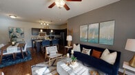 This single-floor residence is designed with an open-concept layout that connects the living area, dining space, and kitchen into one cohesive, functional zone. The living room features wood-style flooring, a ceiling fan with light fixture, and large windows that invite natural light while providing views of the surrounding greenery. A neutral gray accent wall serves as a backdrop for the space, lending a modern, polished feel.

The kitchen is well-appointed with dark espresso cabinetry, granite countertops, and a full suite of stainless steel appliances, including a refrigerator, range, and over-the-range microwave. A built-in wine rack adds a distinctive design detail above the cabinetry. A spacious island with granite countertop offers seating and doubles as a dining area, illuminated by sleek pendant lighting overhead.

The bedrooms feature plush carpeting, ceiling fans, and ample natural light from large windows with blinds. Each bathroom is finished with dark vanity cabinetry, granite countertops, wood-style flooring, and a tub-shower combination with a curved curtain rod. The overall ambiance throughout is contemporary and cohesive, with consistent finishes tying each room together.