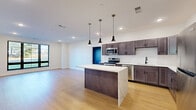 Located at 10 Campus View Ct in Poughkeepsie, NY, this single-floor residence offers a thoughtfully designed layout with contemporary finishes throughout. The open-concept kitchen is a standout feature, showcasing rich dark-toned shaker cabinetry, stainless steel appliances, a white subway tile backsplash, and a generous island topped with striking marble-veined quartz. Three sleek pendant lights hang above the island, complementing the recessed lighting that brightens the space. Light hardwood flooring flows seamlessly through the kitchen and living areas, enhancing the airy, open feel. Large black-framed windows in the living area invite abundant natural light and offer outdoor views of the surrounding greenery. The bedrooms feature plush carpeting and neutral tones, with one room highlighted by a vibrant, colorful botanical mural that serves as a bold artistic focal point. A well-appointed bathroom includes light wood-look flooring, a tub-shower combination with clean white tile surround, a vanity with ample drawer storage, and a large mirror. Spacious walk-in closet storage with built-in shelving and hanging rods adds practical functionality. The overall design is clean, modern, and move-in ready.