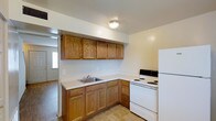 This two-floor residence offers a practical and straightforward layout designed for comfortable everyday living. The kitchen is well-equipped with warm wood-toned cabinetry that lines the upper and lower walls in an L-shaped configuration, providing generous storage space. A built-in sink sits beneath the cabinetry, and the kitchen includes a white electric range and refrigerator. Tile flooring in the kitchen adds durability to the space, while a flush-mount ceiling light provides consistent illumination. An open doorway connects the kitchen to adjacent areas of the home, allowing for easy flow between spaces. The living areas feature wood-style laminate flooring that lends a warm, cohesive feel throughout. Bright white walls keep the interior feeling clean and open, while a ceiling vent ensures efficient climate control. Natural light filters in through a window visible from the main room, contributing to a light and airy atmosphere. The two-floor layout offers separation between living and private spaces, making this residence a functional and versatile home. Overall, the space presents a clean, move-in ready environment with classic finishes and a straightforward design.