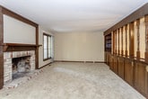 This two-floor home offers a practical and comfortable layout across its multiple levels. The main living area is generously sized, featuring wall-to-wall carpet, exposed ceiling beams, and a classic brick fireplace with a dark wood mantel that serves as the room's focal point. Sliding glass doors and a large window allow natural light to filter in and provide views of the surrounding greenery. Adjacent to the living space, the kitchen is equipped with dark espresso cabinetry, light countertops, a coil-burner electric range, and a full-size refrigerator, all set on light tile flooring. The bedrooms are carpeted and well-proportioned, each with windows that bring in natural light. One bedroom includes direct access to a private bathroom, while a spacious walk-in closet features dual hanging rods and shelving on opposing walls for ample storage. The bathrooms are finished in white tile with extended vanity countertops, large mirrors, under-sink cabinetry, and enclosed shower stalls with sliding glass doors. The lower level provides additional living space, also carpeted, with its own brick fireplace and recessed lighting, offering a versatile area suitable for a variety of uses.