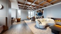 Located at 560 Rideau St in Ottawa, this elegantly designed amenity suite offers a refined and cohesive aesthetic across its generously proportioned single floor. The living room serves as a central showpiece, featuring a striking coffered ceiling with warm wood detailing, a built-in entertainment wall with display shelving, and a linear fireplace that anchors the space. Plush seating arrangements and large windows flood the room with natural light and frame panoramic city views.

The designer kitchen and dining area is a standout highlight, showcasing flat-panel cabinetry in light wood tones, a dramatic arched niche with iridescent mosaic tile backsplash, open floating shelves with ambient LED lighting, and dark countertops. A large marble-topped island with bar seating and elegant pendant lighting adds both function and visual sophistication.

A formal dining room accommodates a substantial oval table surrounded by contemporary upholstered chairs, bathed in natural light from floor-to-ceiling windows with sheer drapery and coffered ceiling detail. A secondary lounge area features a built-in banquette and curated seating nooks with city outlooks. Wide-plank hardwood flooring flows throughout, unifying the space with a warm, modern character.