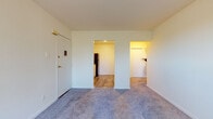 This single-floor residential unit offers a clean, functional layout designed for comfortable everyday living. The main living area is finished with wall-to-wall carpet in a neutral gray tone, providing a warm and understated foundation throughout the space. Crisp white walls create a bright, open atmosphere, and a wide window fitted with horizontal blinds allows natural light to fill the room while offering views of the surrounding greenery. A baseboard heating unit runs along the wall beneath the window, ensuring efficient climate control.

The living area opens directly to the kitchen, which features wood-look vinyl plank flooring for a practical transition between spaces. The kitchen is equipped with white cabinetry, granite-patterned countertops, a stainless sink, and a full-size black refrigerator, providing a functional and cohesive cooking space.

Adjacent to the living area, the bedroom offers comfortable proportions with continued carpeting, white walls, and a set of sliding-door closets that provide ample storage. A baseboard heater and window with blinds mirror the living room, maintaining consistency in both comfort and design throughout the unit. The overall layout is straightforward and well-organized, making efficient use of the available space.