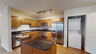 This single-floor residence offers a thoughtfully designed open-concept layout that seamlessly connects the kitchen and living area. The kitchen is a functional centerpiece, featuring warm honey-toned cabinetry, dark granite countertops, stainless steel appliances including a side-by-side refrigerator with ice maker, electric range, microwave, and dishwasher, all set atop durable hardwood-style flooring. A central island with matching countertops provides additional prep and dining space. Track lighting overhead ensures excellent task illumination throughout the kitchen. An in-unit stacked washer and dryer adds everyday convenience. The open living and dining area is carpeted and bathed in natural light through large windows and a sliding glass door that leads to a private balcony. A pendant light fixture serves as an elegant focal point. The bedroom is generously sized, with plush carpeting, a ceiling fan with light, and ample natural light from a large window. A spacious walk-in closet with extensive shelving and hanging rods offers exceptional storage. The bathroom features hardwood-style flooring, a full soaking tub with shower, and clean, neutral finishes throughout. Textured ceilings and neutral wall tones create a cohesive, comfortable atmosphere across the entire space.