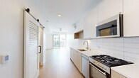 Located at 4135 Park Blvd in San Diego's desirable 92103 neighborhood, this thoughtfully designed unit offers a clean, modern aesthetic throughout. The open-plan kitchen and living area form the heart of the space, finished with light hardwood flooring that runs continuously underfoot. The kitchen is outfitted with white cabinetry, warm wood accents, white subway tile backsplash, stainless steel appliances including a gas range, and a built-in microwave — all centered around a sleek single-basin sink. A sliding louvered barn door adds a stylish architectural touch and provides flexible room division. The living area extends naturally toward a full-width sliding glass door that opens onto a private balcony, flooding the interior with natural light and offering open views of the surrounding San Diego cityscape. The two bathrooms are finished with classic white hexagonal mosaic tile flooring and matte black hardware accents. The primary bathroom features a frameless glass walk-in shower with floor-to-ceiling vertical white tile and brushed nickel fixtures. Additional highlights include a dedicated laundry area, a walk-in closet with built-in shelving and hanging rod, a ceiling fan, and a wall-mounted mini-split system for climate control.