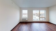 This contemporary single-floor unit is thoughtfully designed with a clean, modern aesthetic throughout. Rich, dark hardwood flooring flows continuously across every room, creating a warm and cohesive feel that contrasts beautifully with the bright white walls and ceilings.

The kitchen is well-appointed with a full suite of stainless steel appliances, including a refrigerator, electric range, and over-the-range microwave. Dark espresso lower cabinetry is paired with crisp white upper cabinets, while dark granite countertops add a sophisticated finishing touch. Open shelving provides additional storage and display space.

The living area is generously sized and filled with natural light from large windows that frame views of the surrounding neighborhood. A wall-mounted HVAC unit ensures year-round comfort in this bright, open space.

Additional rooms include a well-proportioned bedroom with clean white walls and recessed lighting, offering a calm and functional retreat. The bathroom features a dark espresso vanity with a white countertop and integrated sink, complemented by a bathtub and shower combination with a curved curtain rod. A walk-in closet with built-in wire shelving is conveniently accessible directly from the bathroom, providing practical and organized storage. The space as a whole reflects a modern, move-in-ready design with consistent finishes throughout.