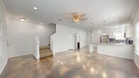 This two-story home in San Antonio, TX offers a thoughtful layout across two floors, combining functional design with modern finishes. The main level features a striking open-concept living and kitchen area unified by polished concrete floors that reflect natural light from multiple windows dressed with white blinds. Crown molding and ceiling fans add a classic touch throughout. The kitchen is well-equipped with white shaker cabinetry, granite countertops, a tile backsplash, stainless steel appliances including a refrigerator, range, microwave, and dishwasher, plus pendant lighting over a peninsula that connects seamlessly to the living area. A dedicated laundry room and a full bathroom are also found on the main level. The staircase, framed by white painted posts, leads to the upper floor where all three bedrooms are located. The carpeted bedrooms are bright and comfortable, each with a ceiling fan and natural light. The generously sized primary bedroom includes a walk-in closet with built-in rods for ample storage. Each of the three bathrooms features clean white finishes, with the upper-level bathrooms offering dark-stained vanities with white countertops and tub-shower combinations on wood-look tile flooring.