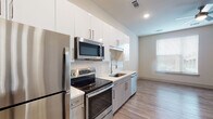 This single-floor studio in Memphis, Tennessee offers a thoughtfully designed layout that maximizes every square foot. The open-concept living and kitchen area is anchored by a well-appointed kitchen featuring a full suite of stainless steel appliances, including a refrigerator, electric range, over-the-range microwave, and dishwasher. White upper cabinetry pairs with wood-toned lower cabinets, complemented by light quartz countertops and a chevron-patterned tile backsplash. A single-basin sink with a modern gooseneck faucet completes the functional workspace.

Light wood-look flooring runs throughout the unit, lending warmth and visual continuity. The main living area receives natural light through a window fitted with horizontal blinds. Recessed lighting provides consistent illumination across the space. A walk-in closet offers notable storage capacity for a studio layout.

The bathroom features a tub-shower combination with full white tile surround, brushed nickel fixtures, a wood-toned vanity, and granite-style countertop. A hallway connects the main living space to the entry door, which includes a keypad lock. The overall aesthetic is clean and contemporary, reflecting modern construction standards with neutral tones throughout.