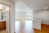 Located on South River Parkway in Portland's vibrant South Waterfront neighborhood, this 2-bedroom, 1-bathroom residence offers a well-designed, light-filled layout across a single floor. The open-concept living and kitchen area is anchored by warm hardwood flooring and large windows that frame urban city views, flooding the space with natural light. The kitchen features light quartz countertops, a peninsula with an integrated sink, warm wood cabinetry, a full suite of white appliances including a range and refrigerator, and ample built-in storage — making it both functional and visually clean. The living room extends naturally from the kitchen, with angled walls and oversized windows creating an airy, dynamic feel. Both bedrooms are carpeted and generously sized, each offering large windows with views of the Portland skyline. The primary bedroom includes a sliding-door closet with built-in shelving for organized storage. The bathroom is well-appointed with a soaking tub and shower combination, a wood-toned vanity with white countertop, and a large mirror. Throughout the residence, the clean white walls, recessed lighting, and consistent finishes create a cohesive, modern aesthetic well-suited to urban living.
