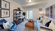 This single-floor residence offers a thoughtfully designed layout that balances comfort and functionality. The open-concept kitchen is a standout feature, showcasing crisp white cabinetry extending to the ceiling, dark quartz countertops, a center island with seating for two, and a full suite of stainless steel appliances including a gas range, microwave, dishwasher, and refrigerator. Light wood-style flooring runs throughout the main living areas, lending warmth and continuity to the space. Double doors off the kitchen provide convenient access to additional storage.

The living area is bright and welcoming, featuring a light-toned sofa accented with layered decorative pillows, a stylish bookshelf, and a set of French doors that invite natural light and offer exterior access. The bedroom is generously proportioned, finished with plush carpeting and natural light from a large window. It comfortably accommodates a king-sized bed alongside nightstands and a dresser, with framed botanical artwork adding a curated touch.

The bathroom is clean and practical, featuring light wood-style flooring consistent with the rest of the home, a tub-shower combination with a curtain, open shelving for décor and storage, and a dark-topped vanity. Throughout the residence, a neutral, contemporary palette creates a calm and cohesive living environment.