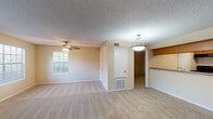 This single-floor residence offers a thoughtfully designed layout with a comfortable, functional flow throughout. The expansive living room is a standout feature, highlighted by a tile-surround fireplace, multiple windows that invite an abundance of natural light, and a ceiling fan for year-round comfort. Soft, neutral-toned carpeting runs through the living spaces, complementing the warm beige walls and textured ceilings that lend a classic character to the interior.

Adjacent to the living room, a dedicated dining area transitions seamlessly into the galley-style kitchen. The kitchen is equipped with rich wood cabinetry, granite-look countertops, a double-basin sink, and black appliances including a refrigerator and range. Durable hardwood-style flooring anchors this space and provides a clean contrast to the surrounding carpeted areas.

The primary bedroom is generously sized and features direct access to a walk-in closet and an en-suite bathroom. The bathroom includes a vanity with wood cabinetry and a well-lit mirror. An additional bedroom provides flexible space and is finished with the same plush carpeting found throughout the home.

The entry foyer, accented with wood-toned flooring, provides a welcoming transition into the main living area, completing a residence that balances practicality with comfort in every detail.
