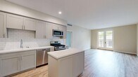 Located at 111 N Madison Ave in Pasadena, CA, this one-bedroom, one-bathroom unit offers a well-designed single-floor layout with a bright, modern aesthetic throughout. The open-concept kitchen and living area serves as the heart of the home, featuring grey shaker cabinetry, white subway tile backsplash, quartz countertops, a center island, and a full suite of stainless steel appliances including a gas range, built-in microwave, dishwasher, and refrigerator. Light hardwood-style flooring runs throughout the main living areas, enhancing the clean, contemporary feel. The living area is bathed in natural light, anchored by French doors that open to a private balcony with outdoor views. The bedroom offers plush carpeting, neutral warm-toned walls, and a window that brings in additional natural light, creating a comfortable and restful retreat. A hallway connects the main living spaces to the bedroom and bathroom. The bathroom is finished with large-format tile flooring, a grey vanity with a white countertop, a framed mirror, and a tub/shower combination with tile surround. The overall ambiance is clean, modern, and move-in ready, suited for comfortable urban living in the heart of Pasadena.