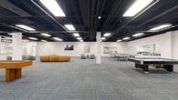 Located at 900 Crane Dr in DeKalb, Illinois, this generously scaled single-floor space offers a dynamic blend of recreation and relaxed gathering areas. The open-plan layout is defined by an exposed black ceiling grid fitted with bright recessed panel lighting, which illuminates the entire floor evenly and contributes to the industrial-modern aesthetic. Patterned commercial carpet tiles in muted blue-grey tones cover the floor throughout, providing both durability and visual cohesion.

The recreational zone is prominently anchored by multiple pool tables and ping pong tables, making it well-suited for social and leisure programming. Full-wall mirrors along one side of the recreation area amplify the sense of openness. A dedicated lounge area features contemporary curved grey seating pods and accent side tables, offering a comfortable retreat for casual conversation.

A floor-to-ceiling glass partition wall with aluminum framing separates the main open area from adjacent spaces, maintaining visual connectivity while defining distinct zones. Along the glass wall, counter-height bar tables with leather stools provide informal seating with views into the adjoining area. White structural columns are distributed throughout the floor, complementing the clean white walls.

A wall-mounted flat-screen television and carefully selected artwork add finishing touches, while the expansive footprint makes this space highly adaptable for a variety of community, corporate, or recreational uses.